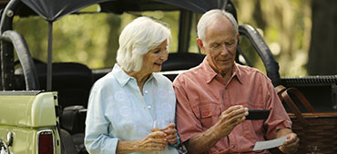 Couple sitting on their vehicle making a check deposit using their phone.