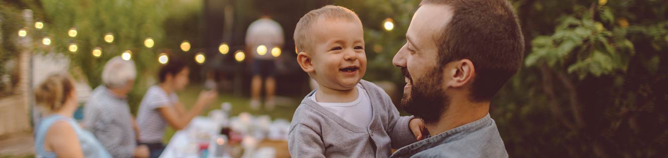 Young man holding his child at an outdoor dinner.