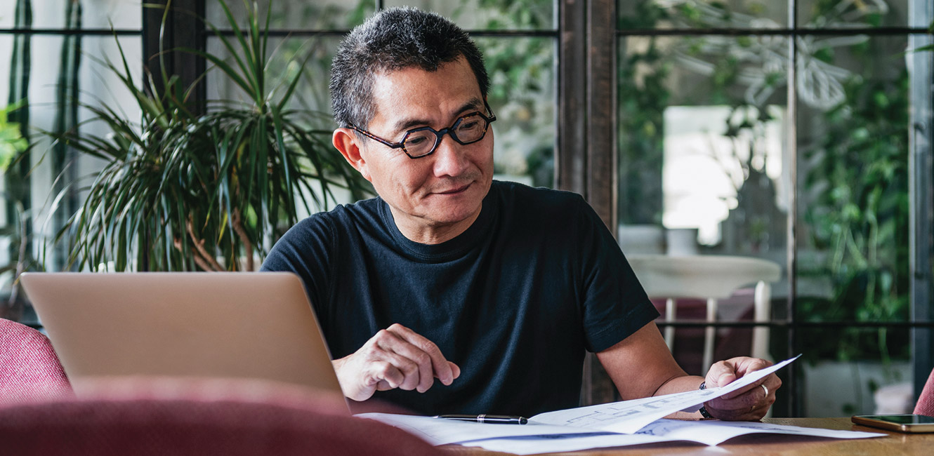 Businessman reading documents in front of laptop.